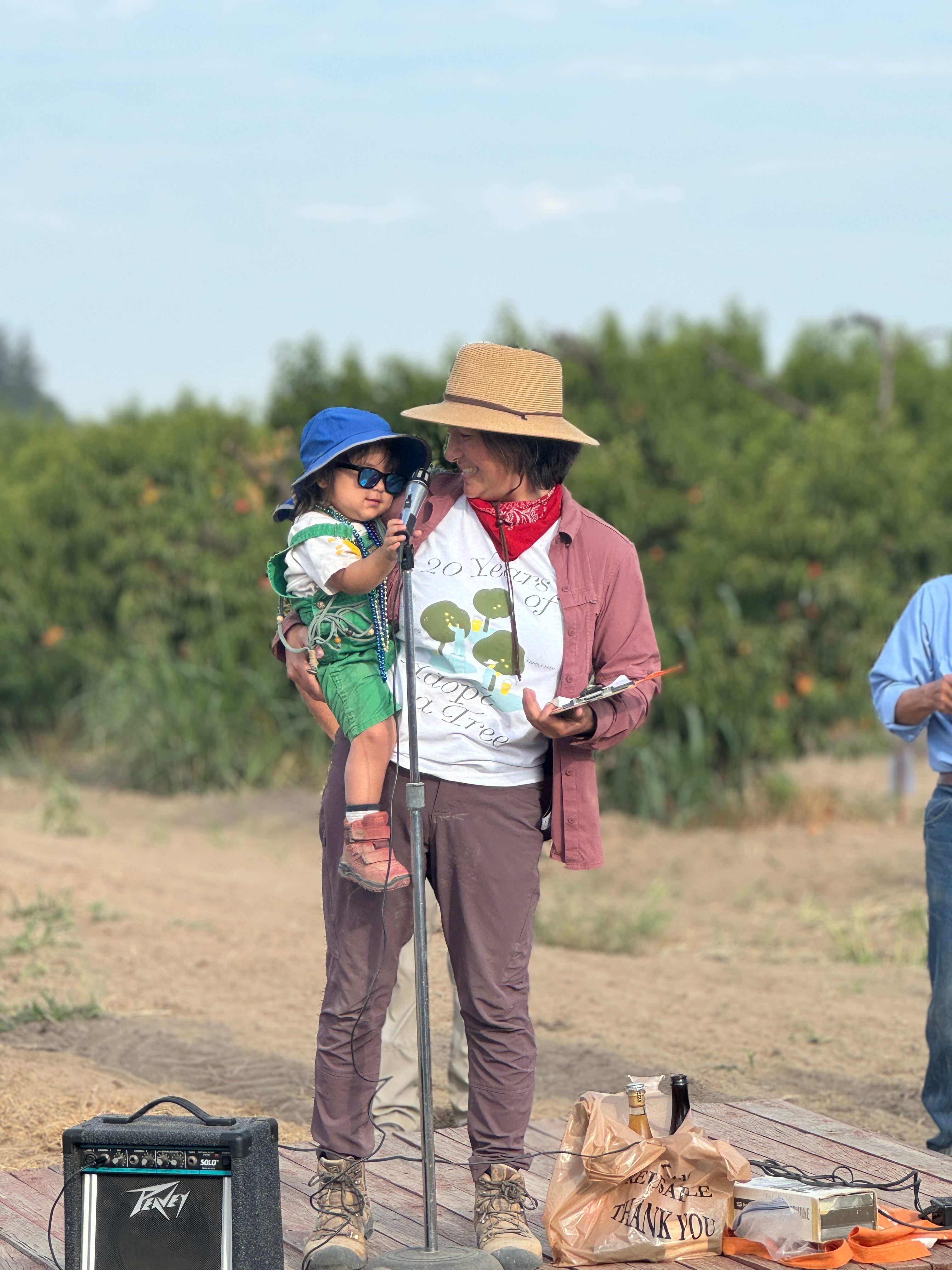 Nikiko gives a speech on harvest day with her daughter, Nunziata, at her hip.