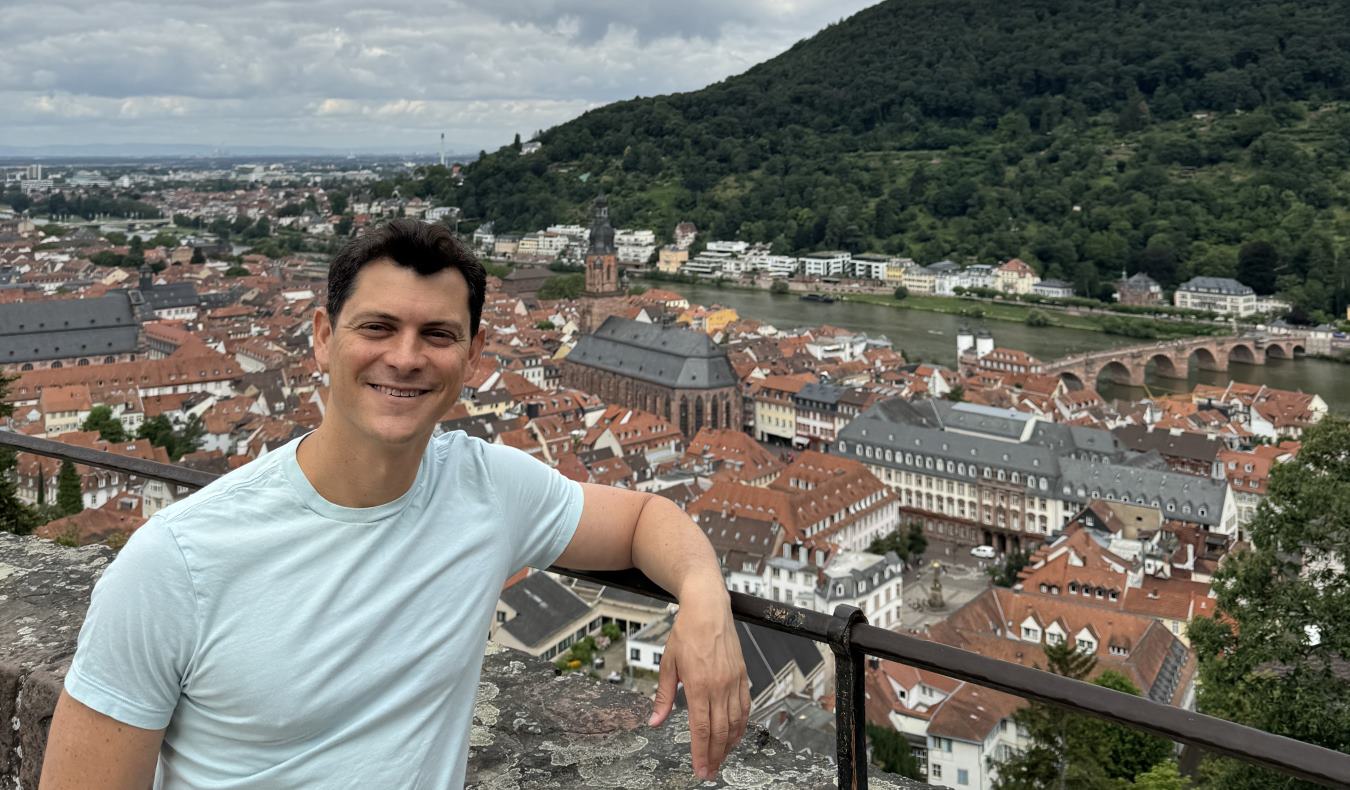 Nomadic Matt posing for a photo on a sunny day with the cityscape of Heidelberg, Germany in the background