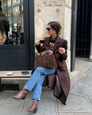 Woman wears brown coat, argyle knit, blue jeans and brown boots