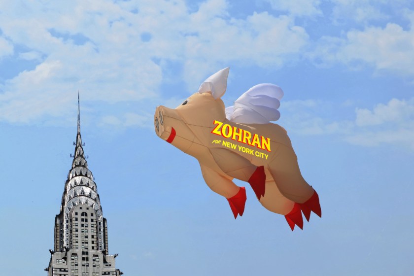 An inflatable pig balloon against a blue sky, bearing the Zohran for Mayor logo. The Chrysler Building sits to one side.