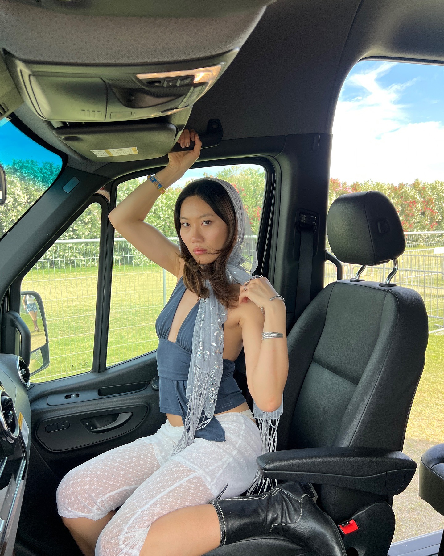 Influencer @vivianyrl poses in a car wearing sheer white capri pants with a dark blue halterneck top and a sheer scarf draped around her hair.