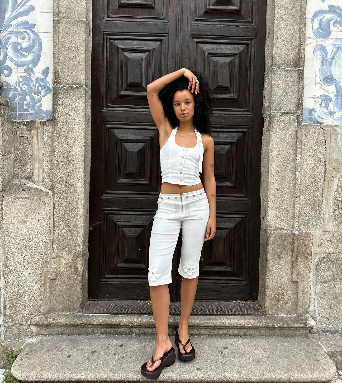 Influencer stands on a step outside wearing white carpi pants with a matching white top and platform flip-flop shoes.
