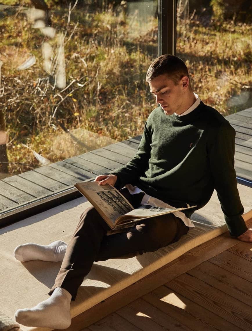 man sitting down by a window reading a book