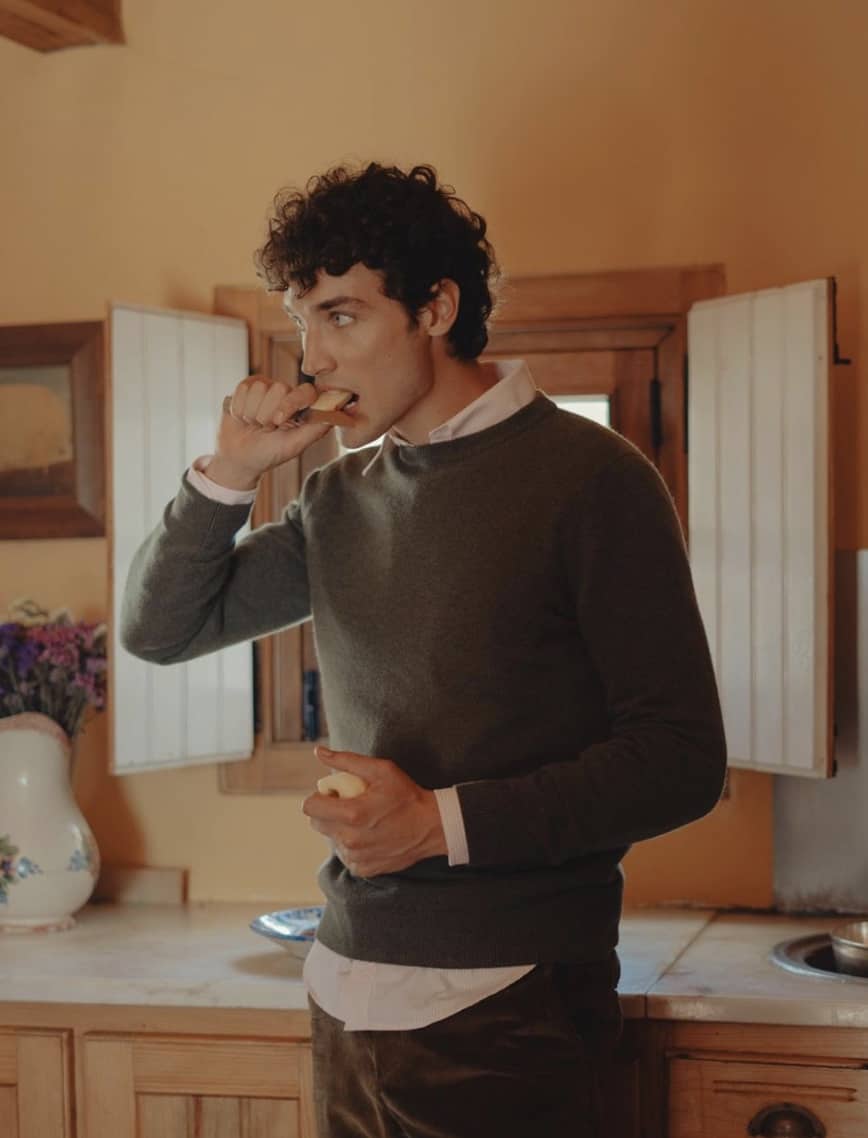 man standing in a kitchen, cutting and eating an apple