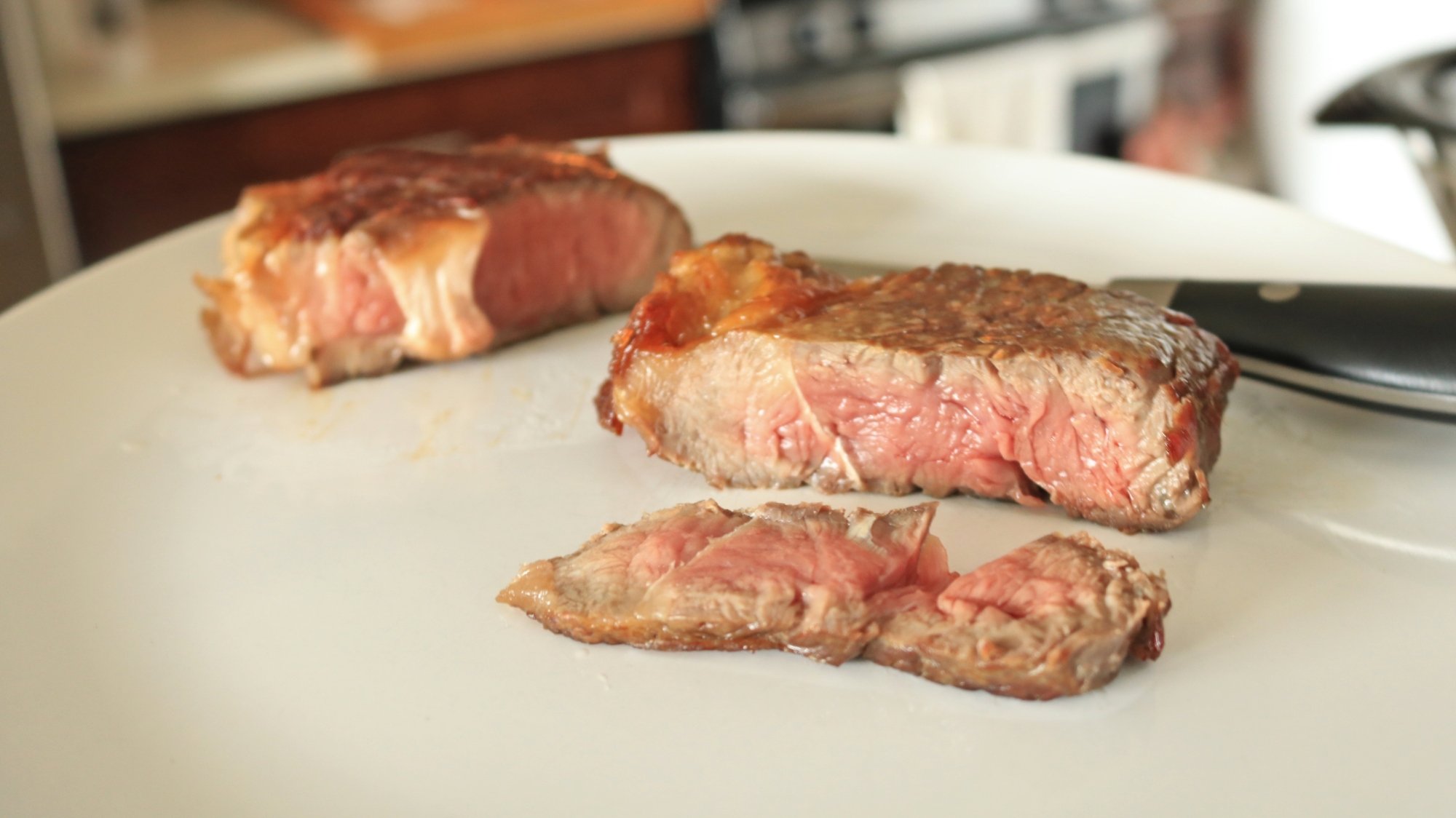 Two small steaks on a plate and one has been sliced.