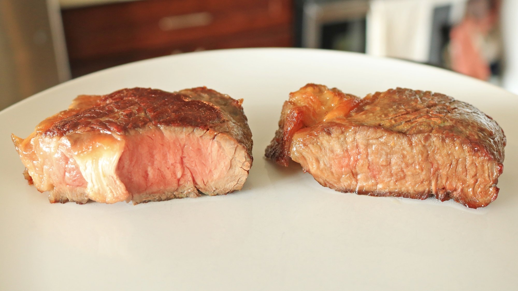 Two steaks on a plate and one is more cooked than the other.