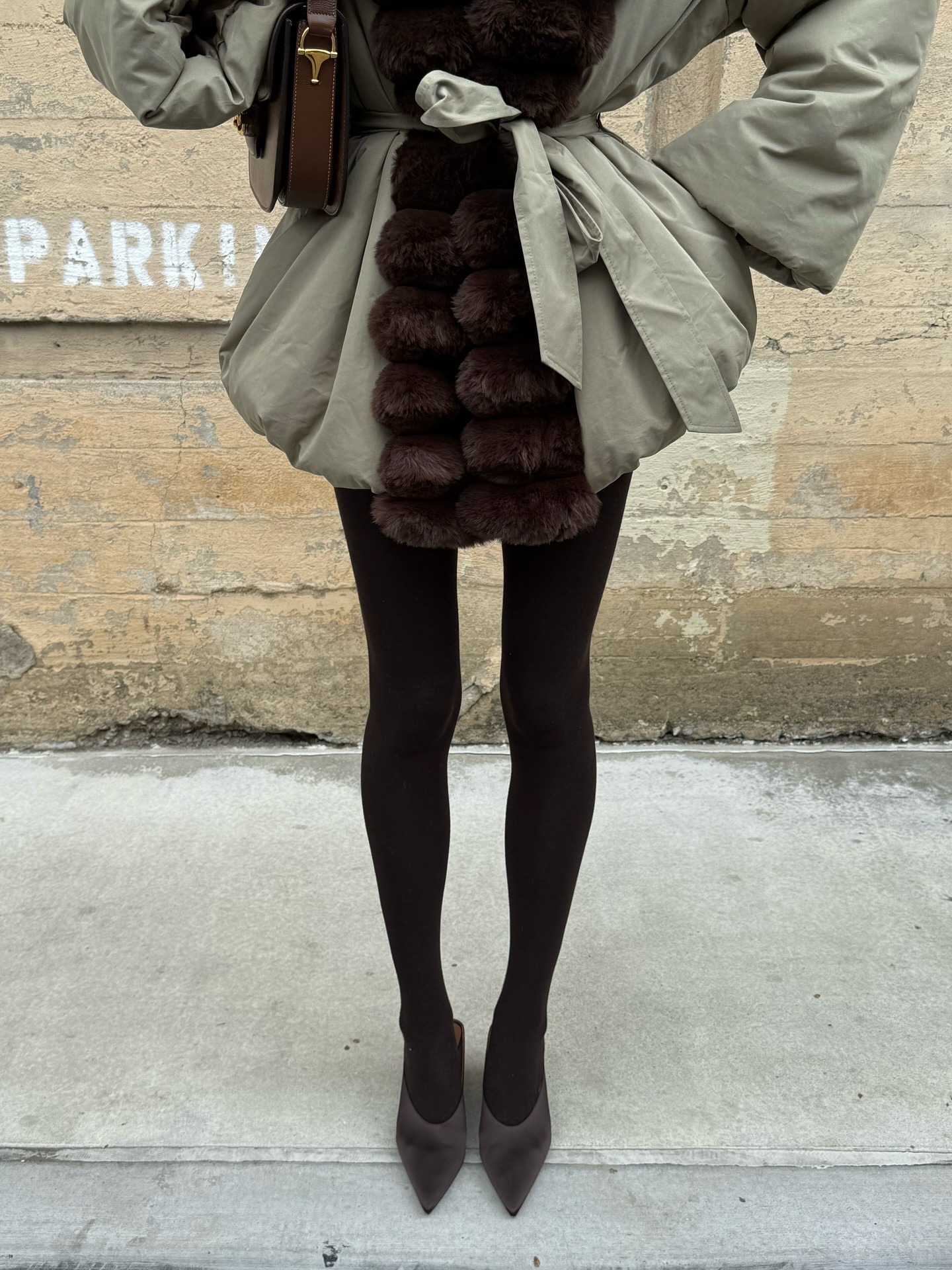 Elsa Hosk wearing a fur-trimmed parka, brown tights, and brown Alaia satin mules